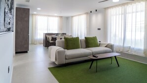 A modern living room with a sofa, a coffee table, and a dining area in the background. - Luxury Apartment in La Zenia (Orihuela)