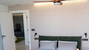 A modern bedroom with a large bed, a ceiling fan, and a view of a bathroom. - Luxury Apartment in La Zenia (Orihuela)