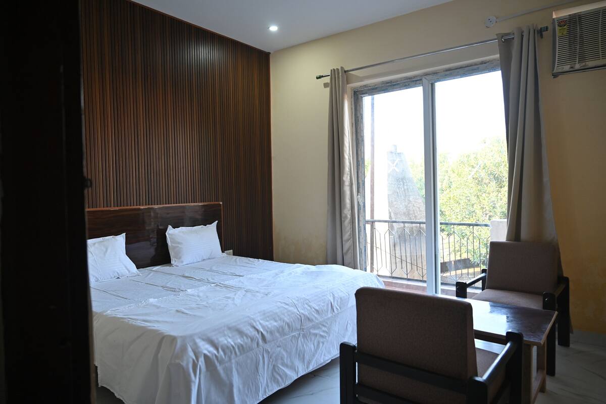 Hotelkamer met groot bed, houten hoofdbord, balkon met stoel en raam met gordijnen.