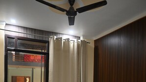 Habitación de hotel con cama, ventilador de techo, ventana con cortinas y vista a un balcón.