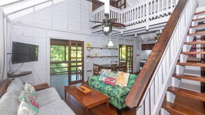 A spacious living area with a wooden staircase, a ceiling fan, and a television mounted on the wall.