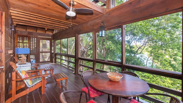 A wooden deck with a table and chairs, large windows, and a ceiling fan.