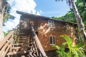 Une cabane en bois avec un escalier menant à l’entrée, entourée d’une végétation luxuriante.