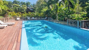 A wooden deck with a clear blue pool surrounded by lush greenery and a wooden fence.