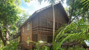 A wooden house surrounded by lush greenery and a tree branch.