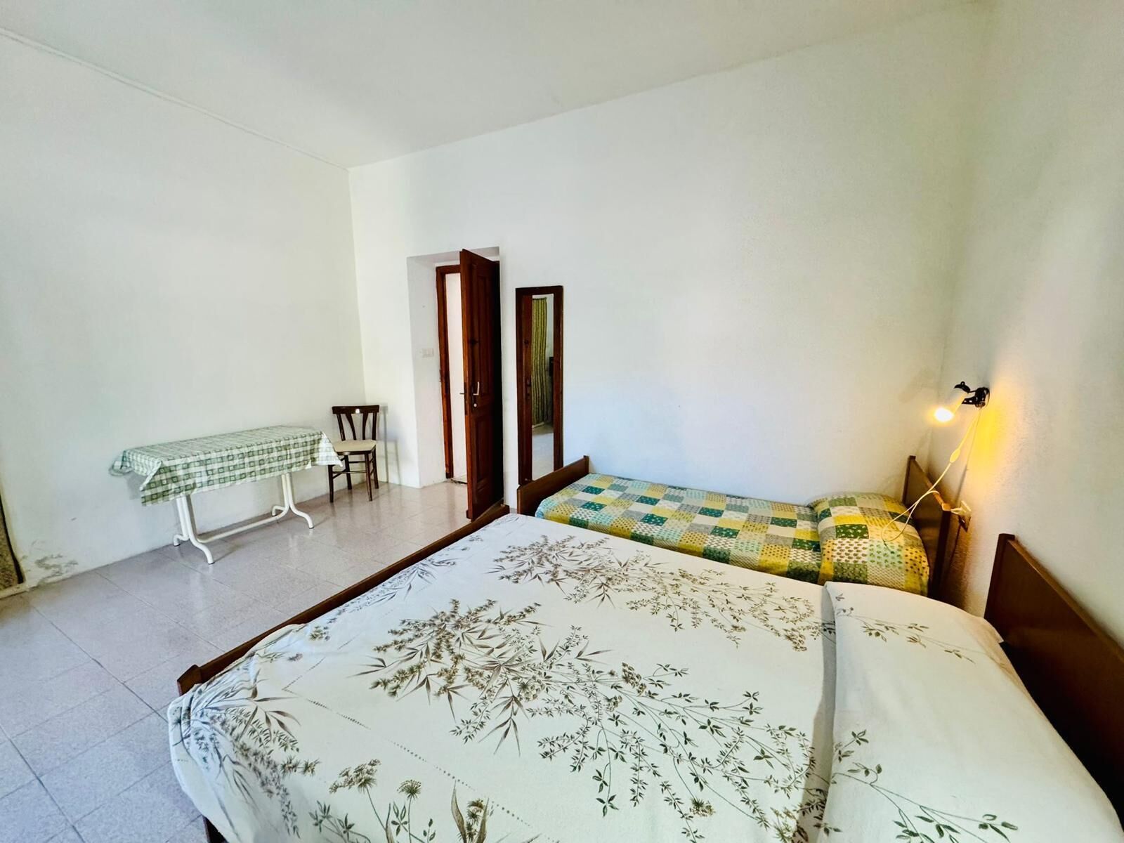 Une chambre à coucher avec un lit, une petite table recouverte d’une nappe à carreaux et une chaise.
