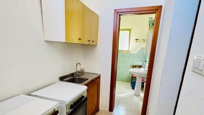 Μια μικρή, λειτουργική κουζίνα με λευκό πάγκο, ξύλινα ντουλάπια και εντοιχισμένο φούρνο.