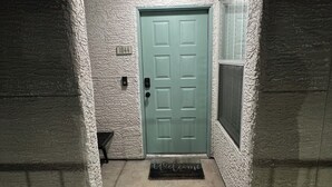 Ein schmaler Eingang mit einer grünen Tür, einer Fußmatte und einem kleinen Fenster zur Rechten.
