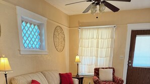A living room with a beige sofa, a patterned armchair, a red ottoman, a patterned armchair, a ceiling fan, a window with a lattice, and a door with a window. - Hidden Gem: Cozy, please read full description (Cleveland)