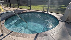Ein Whirlpool mit einer Metallleiter, umgeben von einer gefliesten Terrasse und einer Glasumrandung.