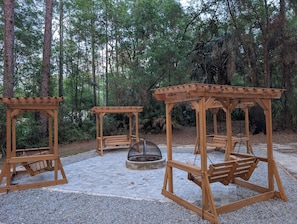 Une structure en bois en forme de gazebo, située dans une zone boisée et dotée d’un sol en gravier.