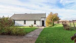 Une maison blanche avec un toit gris, une allée pavée et une cour verdoyante entourée d’une clôture en bois.