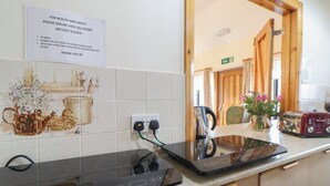 Une cuisine équipée d’une plaque de cuisson à induction moderne, d’une bouilloire et d’un grille-pain. Un panneau affiché au mur rappelle qu’il est important de garder les portes fermées pour des raisons de santé et de sécurité.