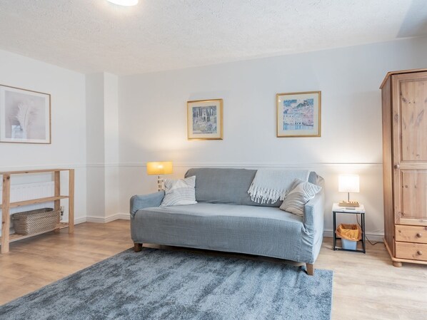 A living room with a grey sofa, a wooden cabinet, and a small table with a lamp.