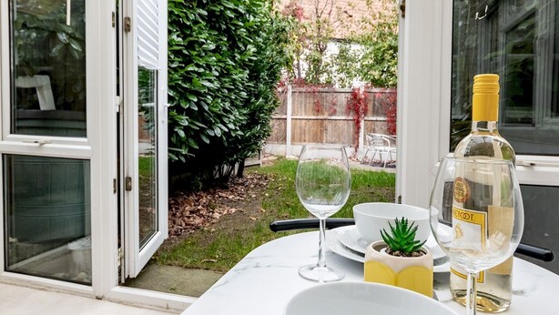 A dining area with a table set for two, featuring a white bowl, a wine glass, and a bottle of liquor. - Pass the Keys | Cosy home | Basildon | Ideal for contractors (Basildon)
