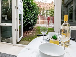 A dining area with a table set for two, featuring a white bowl, a wine glass, and a bottle of liquor.