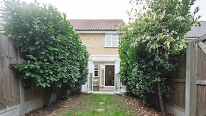 A backyard with a wooden fence, a brick house, and a small garden area with a pathway. - Pass the Keys | Cosy home | Basildon | Ideal for contractors (Basildon)