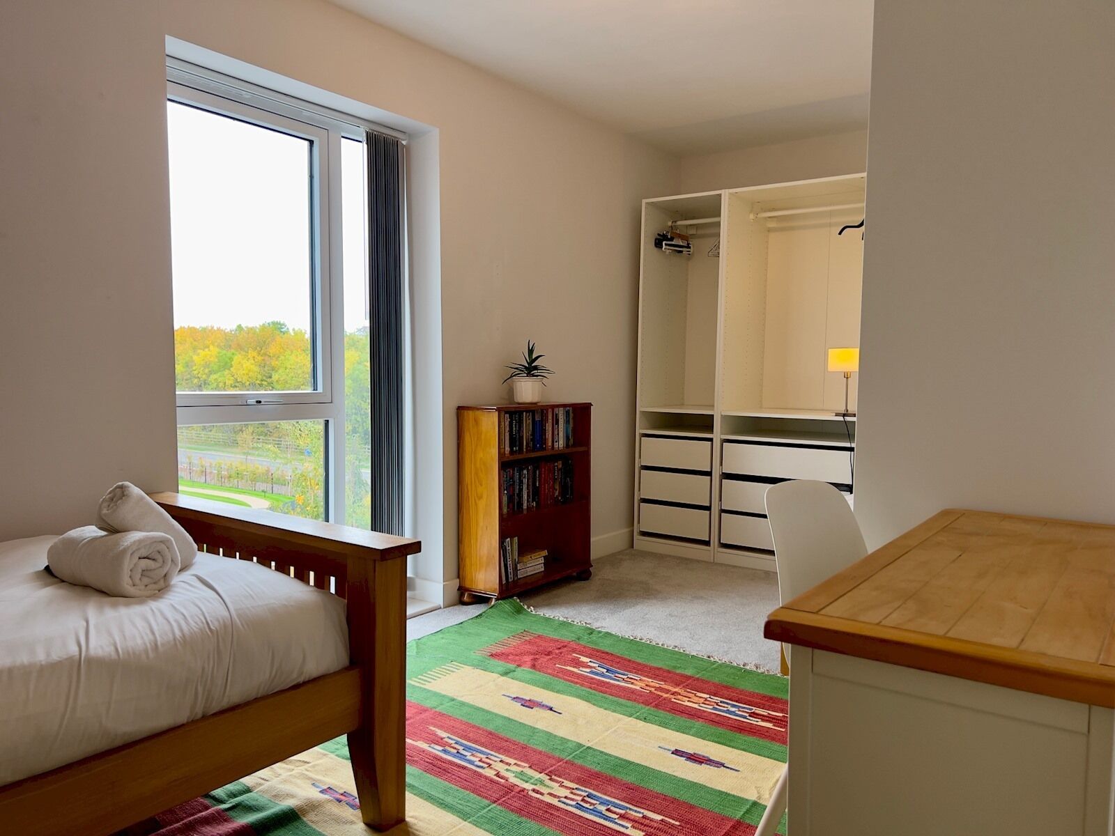 A bedroom with a bed, a window, a bookshelf, a desk, and a closet.