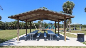 A covered picnic area with benches and a playground in the background.