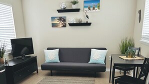 A living room with a dark grey sofa, a flat-screen TV on a black stand, a dining table with chairs, and a small dining area.