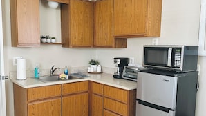 A compact kitchen with wooden cabinets, a stainless steel refrigerator, a microwave, and a coffee maker.