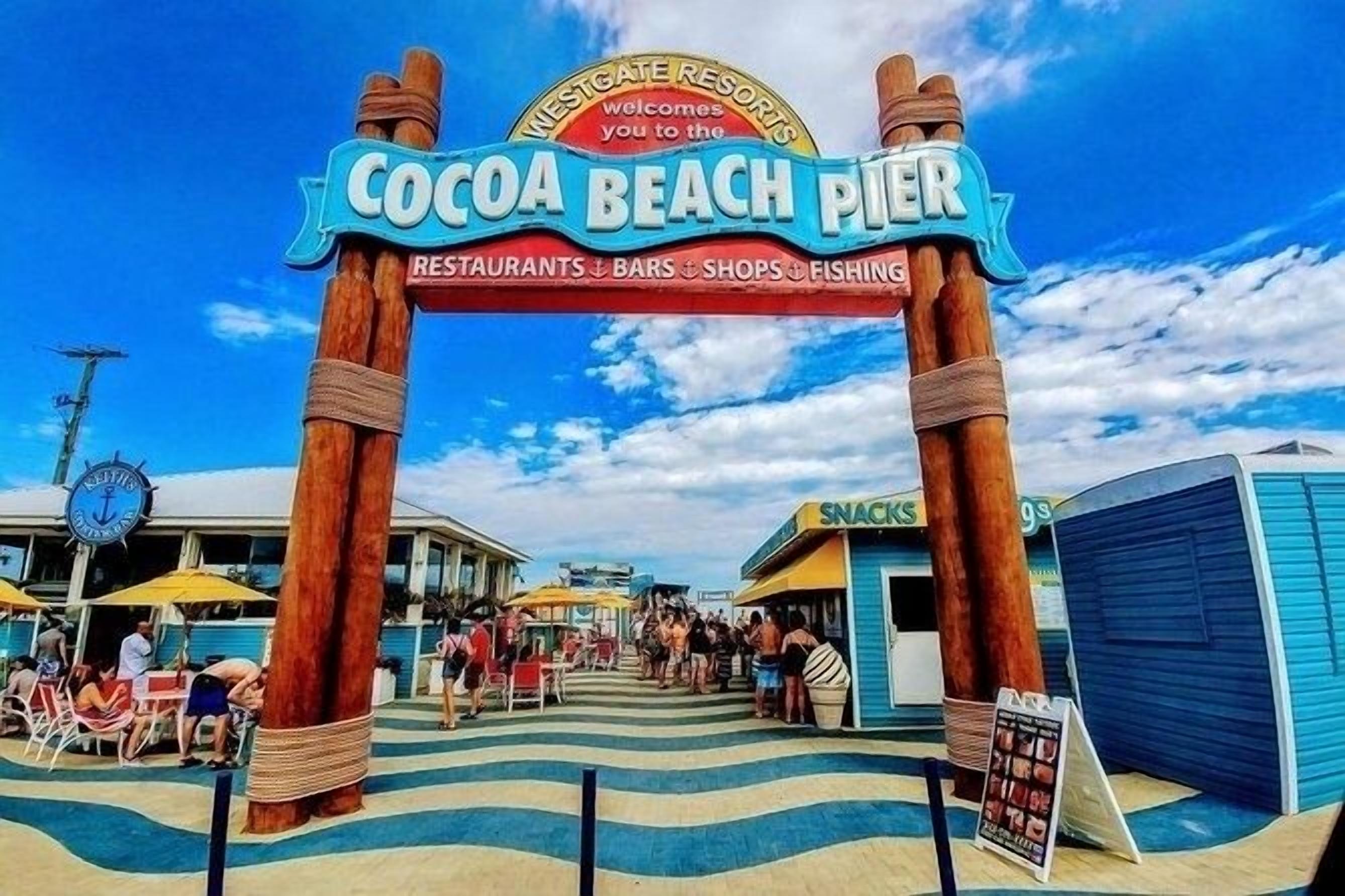 Entrada de um píer à beira-mar com uma placa indicando 'Cocoa Beach Pier' e um relógio.