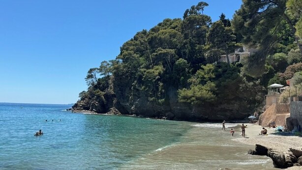 Une plage à l’eau claire, avec un rivage rocheux et une végétation dense.
