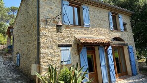 Un bâtiment en pierre avec un toit en tuiles, de nombreuses fenêtres équipées de volets et un petit porche.