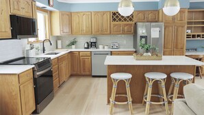 A modern kitchen with wooden cabinets, stainless steel appliances, and a central island with bar stools. - Grand Isle Lakehouse with Hot Tub (Grand Isle)