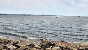A calm body of water with a rocky shoreline in the foreground and distant landforms under a clear sky. - Grand Isle Lakehouse with Hot Tub (Grand Isle)
