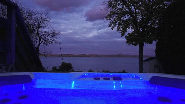 An outdoor swimming pool with blue lighting, surrounded by trees and overlooking a body of water. - Grand Isle Lakehouse with Hot Tub (Grand Isle)