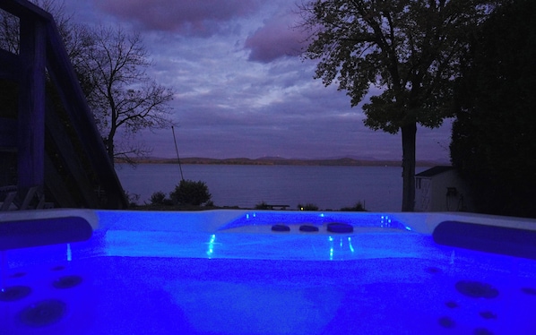 Ein Außenpool mit blauer Beleuchtung, umgeben von Bäumen und mit Blick auf ein Gewässer.