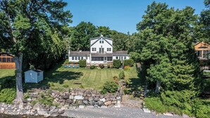 A large, two-story house with a front lawn, surrounded by trees and a stone wall. - Grand Isle Lakehouse with Hot Tub (Grand Isle)