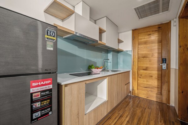 A modern kitchen with a stainless steel refrigerator, wooden cabinets, a built-in sink, and a wooden door.