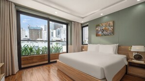 A modern hotel room with a large bed, wooden flooring, a city view, and a painting on the wall. - Happy House Hotel & Apartment (Da Nang)
