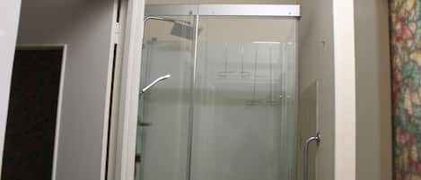 A glass-enclosed shower with a showerhead and handrails.