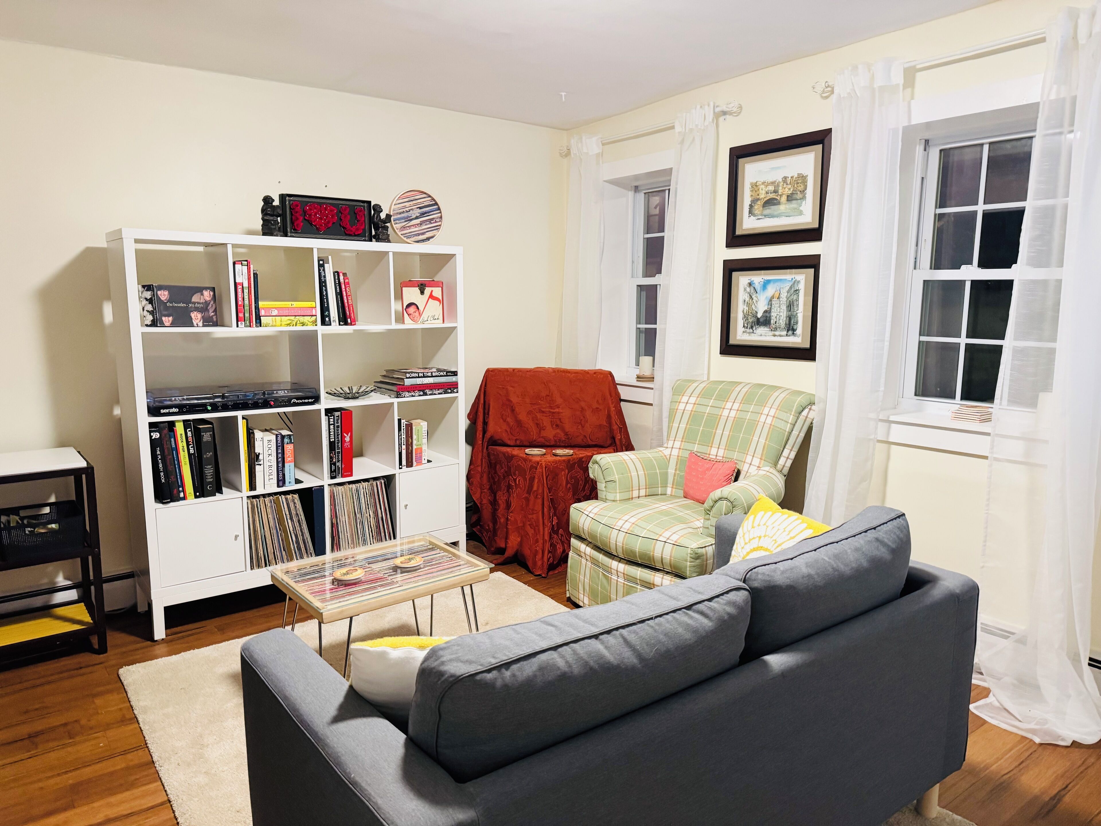A living room with a grey sofa, a white bookshelf, a red armchair, and a small table.