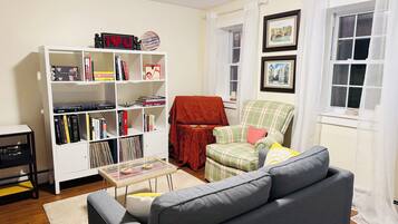 A living room with a grey sofa, a white bookshelf, a red armchair, and a small table.