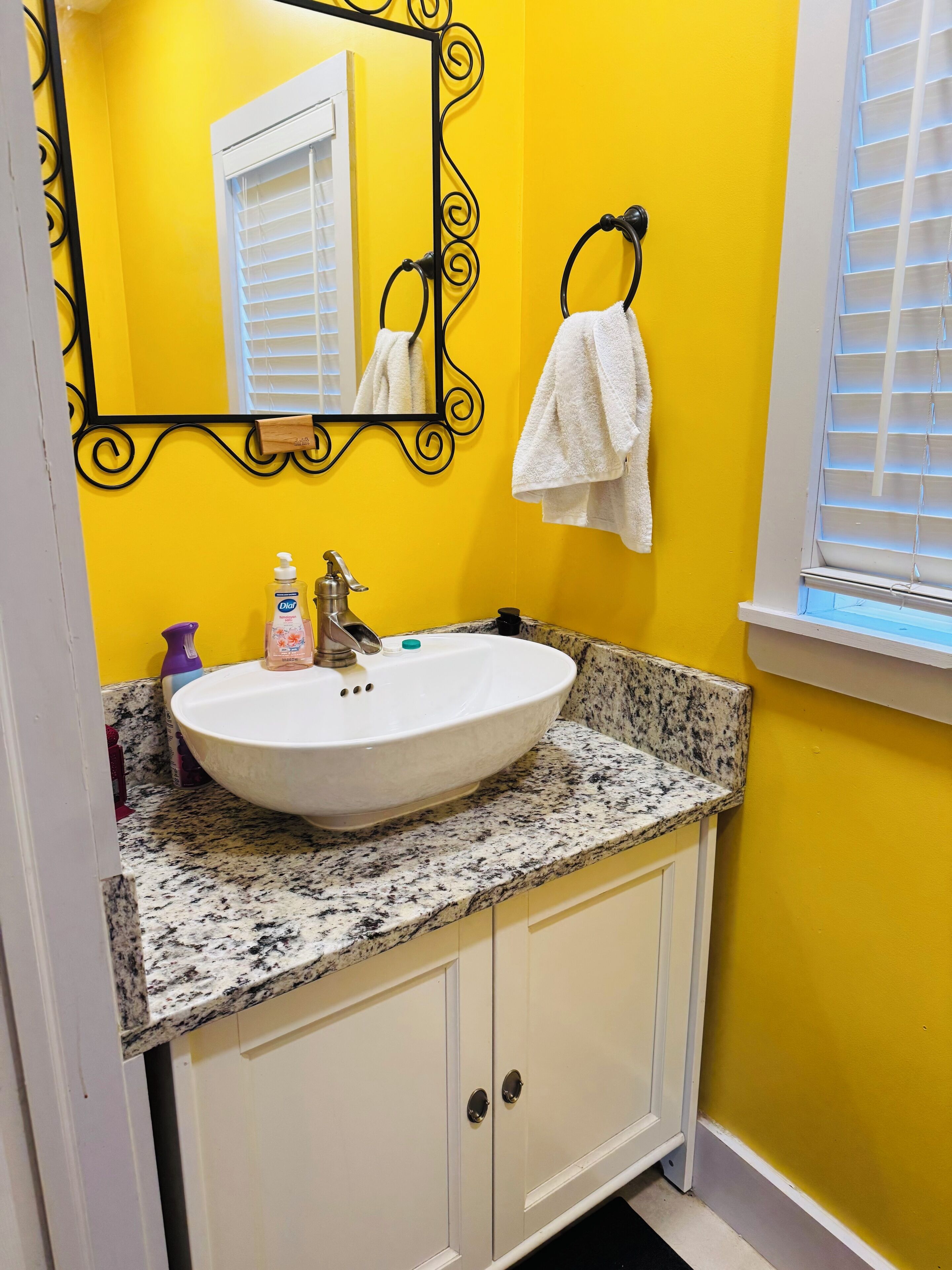 Un baño con lavamanos blanco, encimera de granito y paredes amarillas.