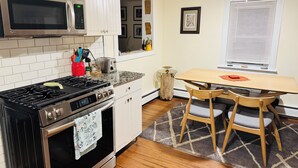 A modern kitchen with a stove, microwave, and oven. There is a dining table with chairs and a window with blinds. - The Quiet House on Main Street minutes from Everywhere (Shrewsbury)