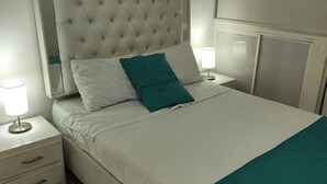 A neatly made bed with a white headboard and teal throw pillows, a bedside table with a lamp, and a digital thermostat on the bed. - Cozy 2nd Floor Apartment in Heart of Cartagena (Cartagena)