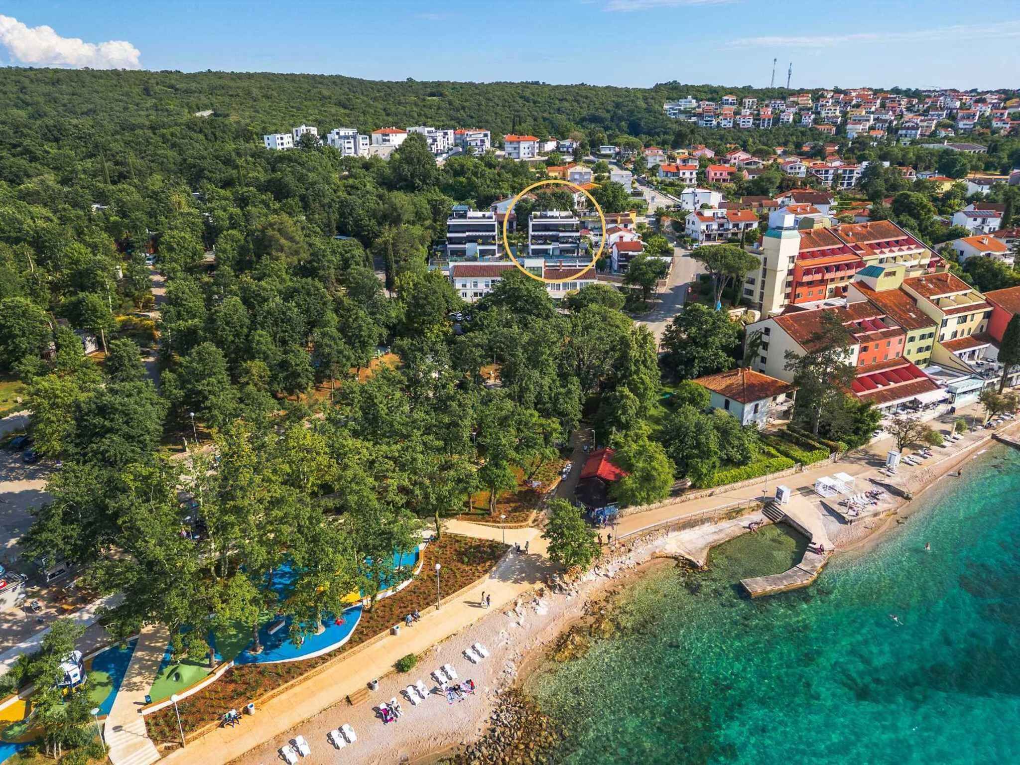 An aerial view of a coastal town with a beach, clear waters, and a mix of residential buildings.