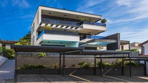 A modern multi-story building with balconies, a covered entrance, and a clear sky. - Holiday apartment Luxurious flat with a beautiful terrace overlooking the sea (Njivice)