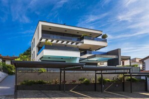 Un edificio moderno de varios pisos con balcones, una entrada cubierta y cielo despejado.