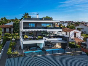 Una casa moderna de dos pisos con piscina en la azotea, un balcón y vistas del vecindario circundante.