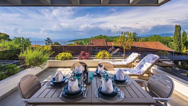 A dining table set outdoors with a view of the sea and hills. - Holiday apartment Luxurious flat with a beautiful terrace overlooking the sea (Njivice)