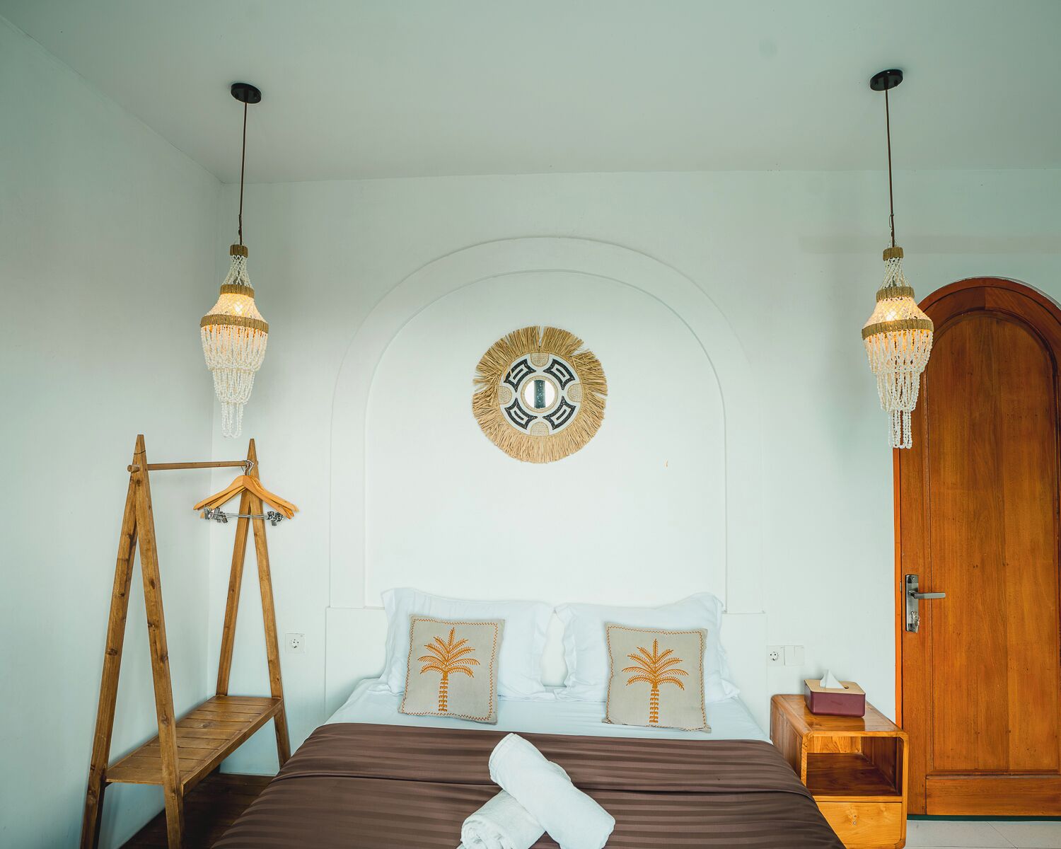 A bedroom with a bed, wooden wardrobe, hanging lights, and a wall-mounted decorative piece.
