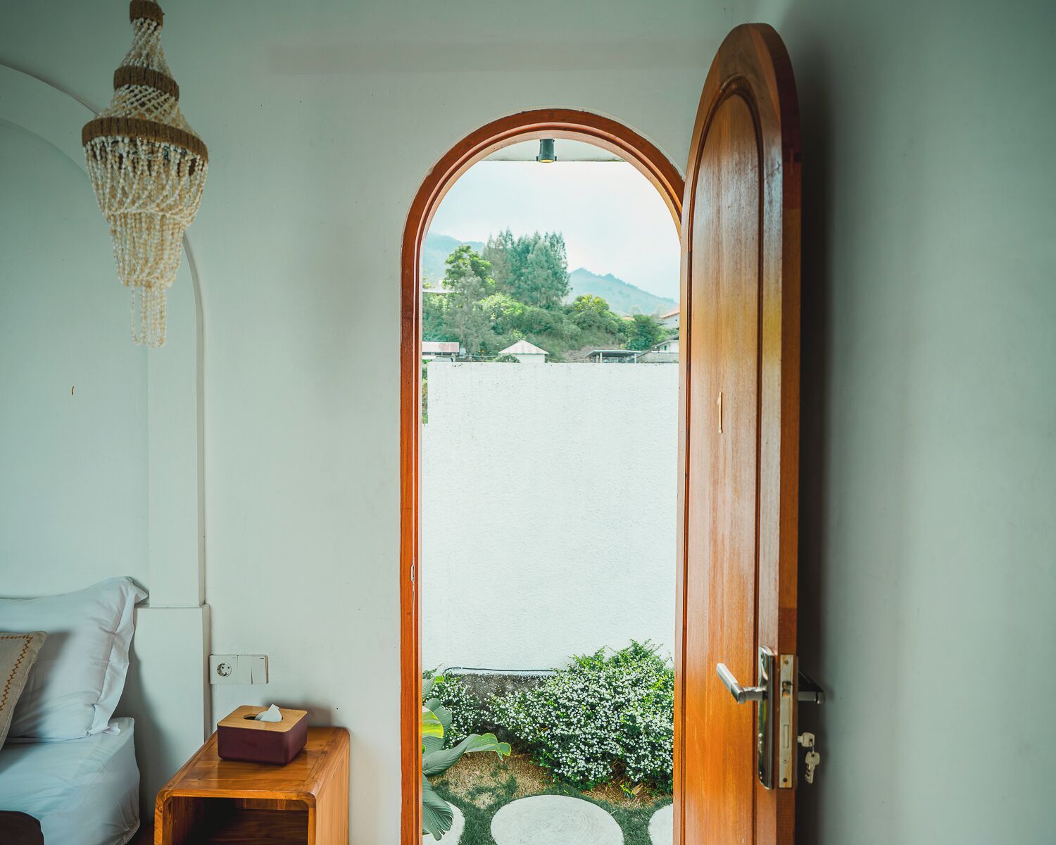 A room with a wooden door leading to a balcony with a view of a body of water and greenery.