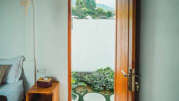A room with a wooden door leading to a balcony with a view of a body of water and greenery.