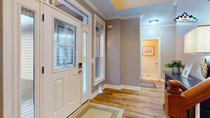 A hallway with a wooden floor, a door with a glass panel, a staircase, and a reception desk with a plant. - Breeze on Inn • Deck, Firepit, & Game Room (Sugar Mountain)